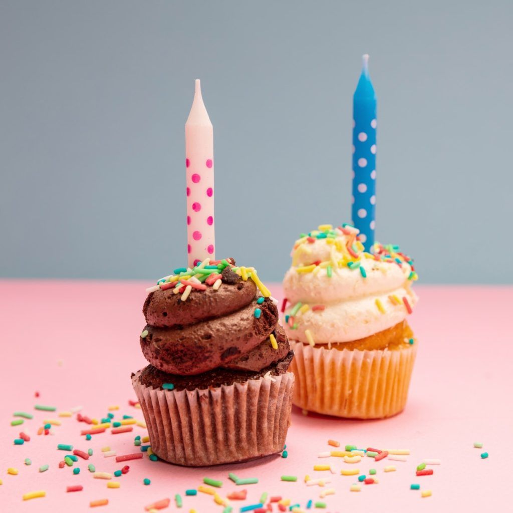 Two birthday cupcakes with candles on blue and pink pastel background, copy space.