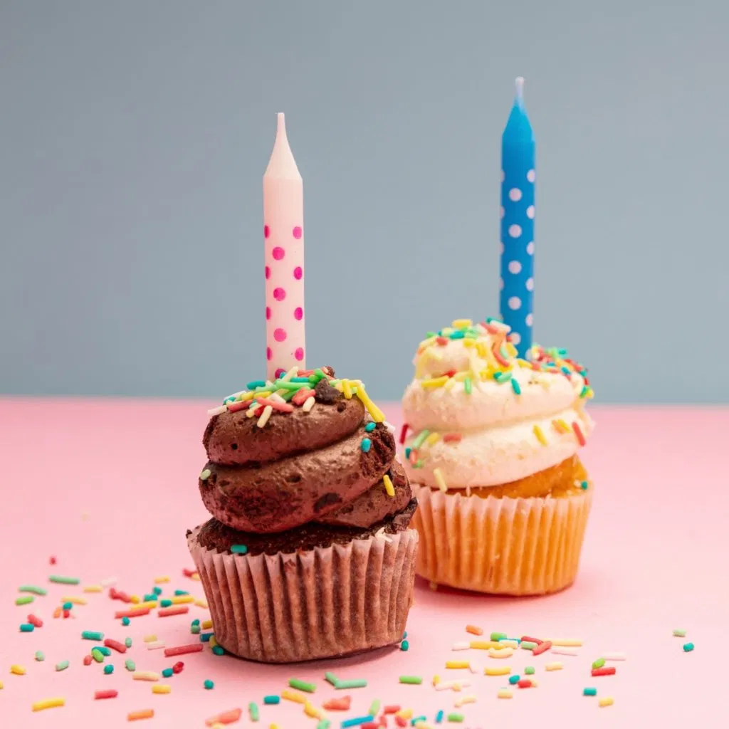Two birthday cupcakes with candles on blue and pink pastel background, copy space.