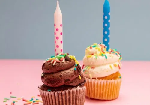 Two birthday cupcakes with candles on blue and pink pastel background, copy space.